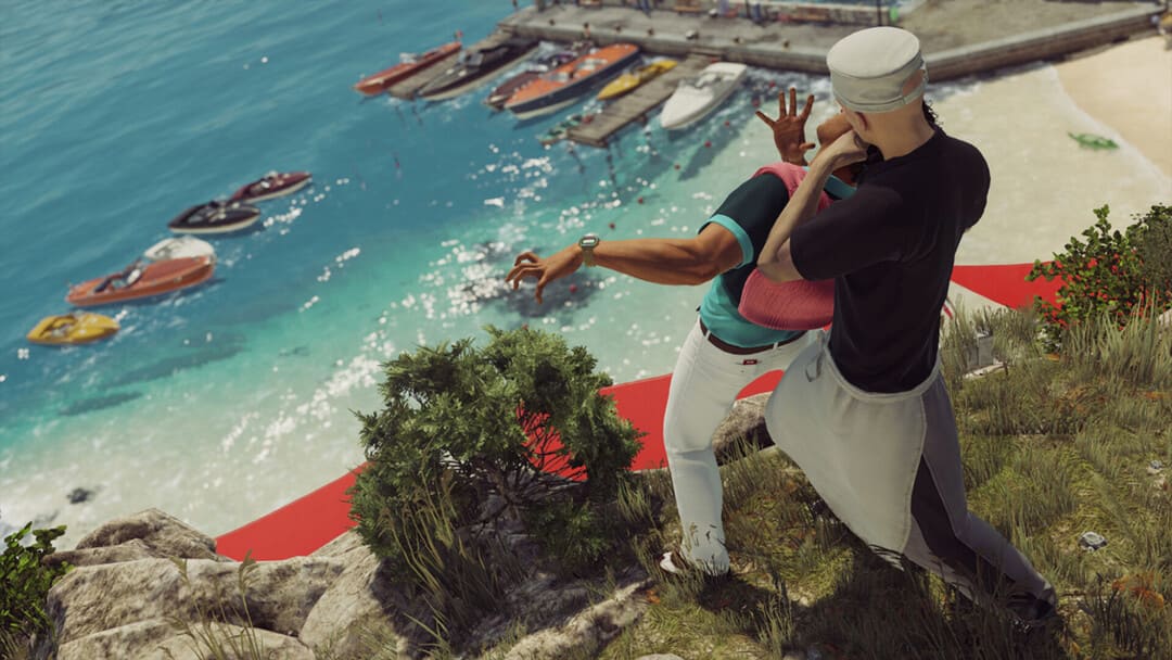 게임의 스크린 샷 Hitman World of Assassination의 스크린 샷은 백그라운드에서 스피드 보트를 곁들인 해변 절벽에서 남자를 죽이는 검은 티셔츠를 입은 남자를 보여주는 남자를 보여줍니다.